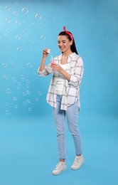 Young woman blowing soap bubbles on light blue background