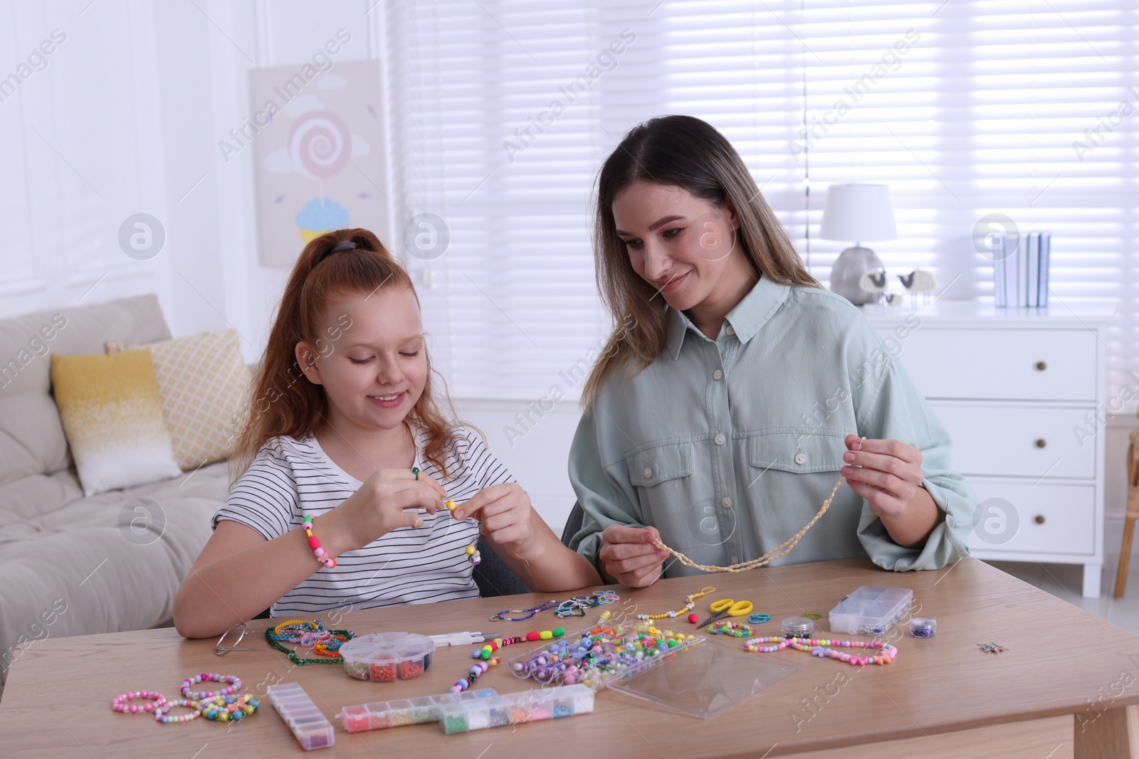 Photo of Happy mother with her daughter making beaded jewelry at home