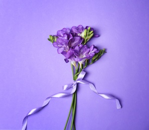 Photo of Beautiful freesia flowers with ribbon on color background