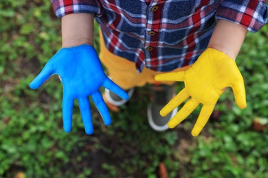 Photo of Little boy with hands painted in Ukrainian flag colors outdoors, top view. Love Ukraine concept