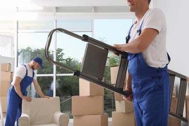 Photo of Moving service employees with ladder and cardboard boxes in room, closeup