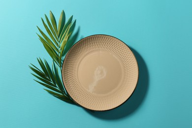 Photo of Ceramic plate and green leaves on turquoise background, flat lay