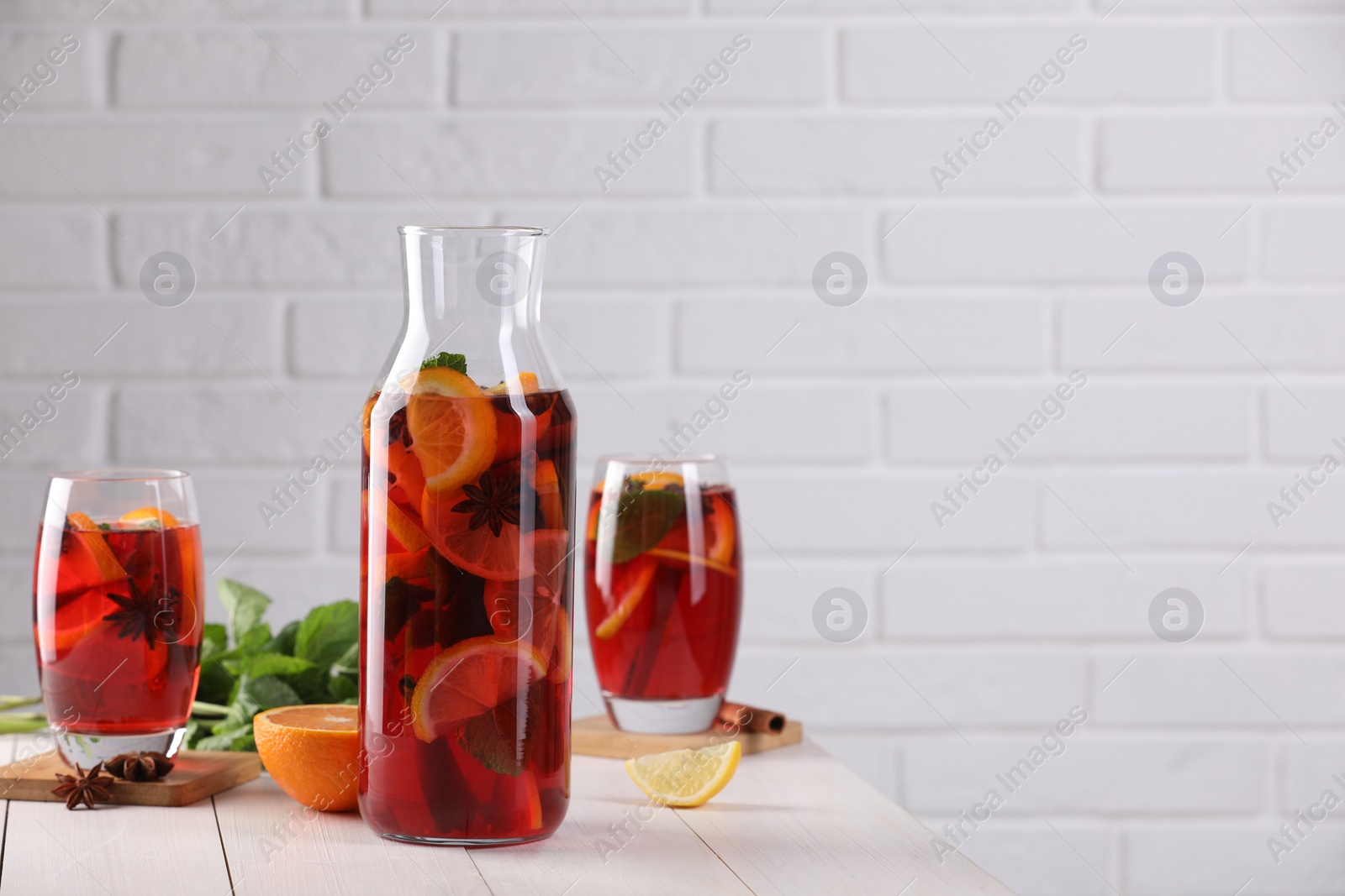Photo of Delicious punch drink and ingredients on white wooden table. Space for text