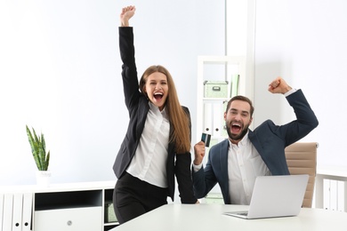 Photo of Emotional young people with credit card and laptop celebrating victory in office