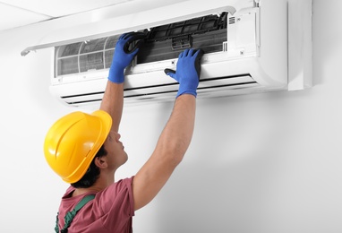Photo of Male technician checking air conditioner indoors