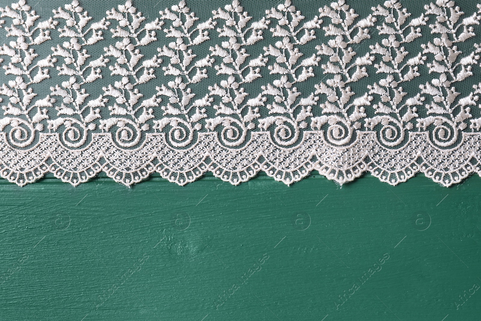 Photo of Beige lace on green wooden table, top view. Space for text