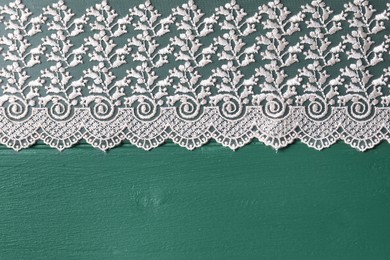 Photo of Beige lace on green wooden table, top view. Space for text