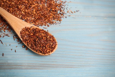 Photo of Dry rooibos leaves and spoon on turquoise wooden table, closeup. Space for text