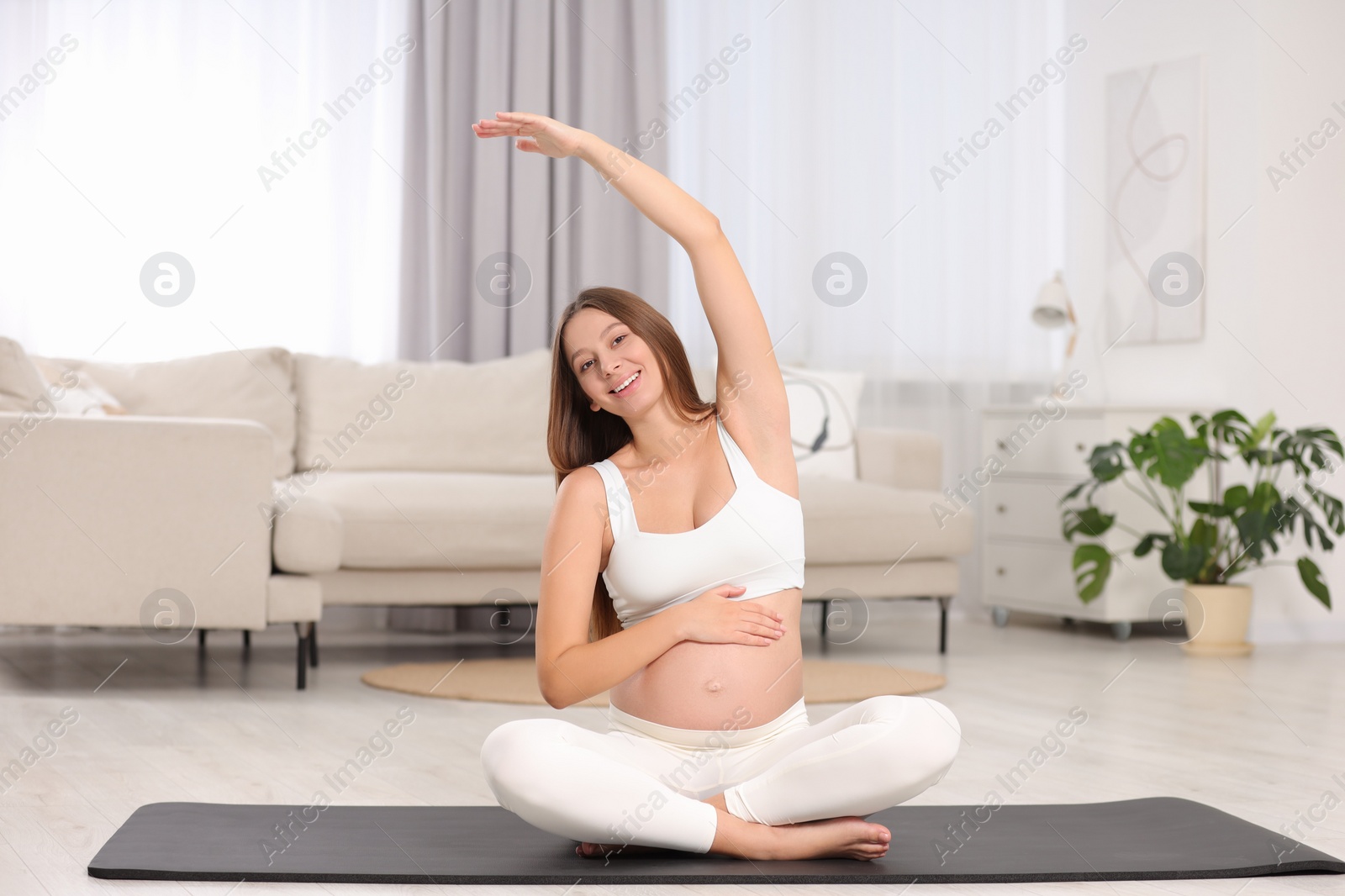 Photo of Pregnant woman stretching on yoga mat at home