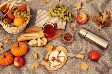 Image of Blanket with picnic basket, snacks and autumn leaves, flat lay