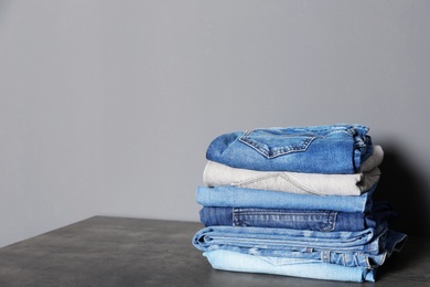 Photo of Stack of different jeans on  table against gray background. Space for text