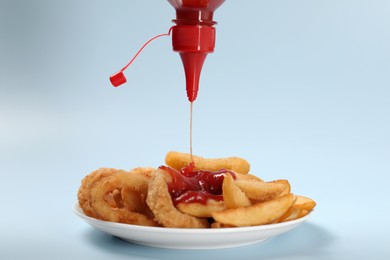 Photo of Pouring ketchup onto tasty baked potato and fried onion rings against light blue background