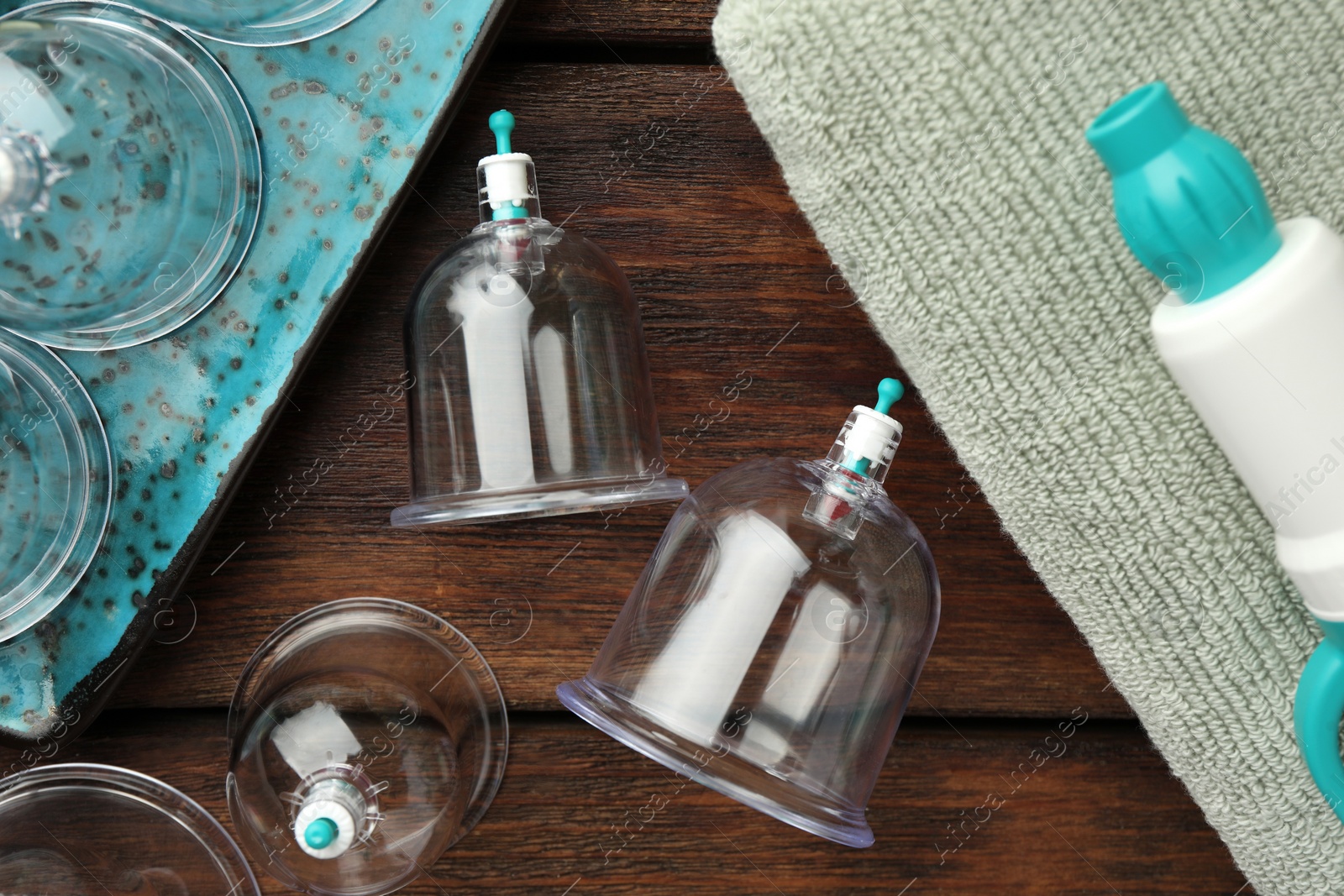 Photo of Cupping therapy. Plastic cups, hand pump and towel on wooden table, flat lay