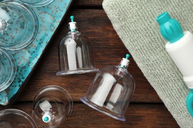 Photo of Cupping therapy. Plastic cups, hand pump and towel on wooden table, flat lay