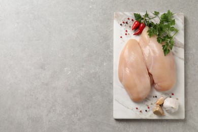 Photo of Raw chicken breasts and ingredients on light grey table, top view. Space for text