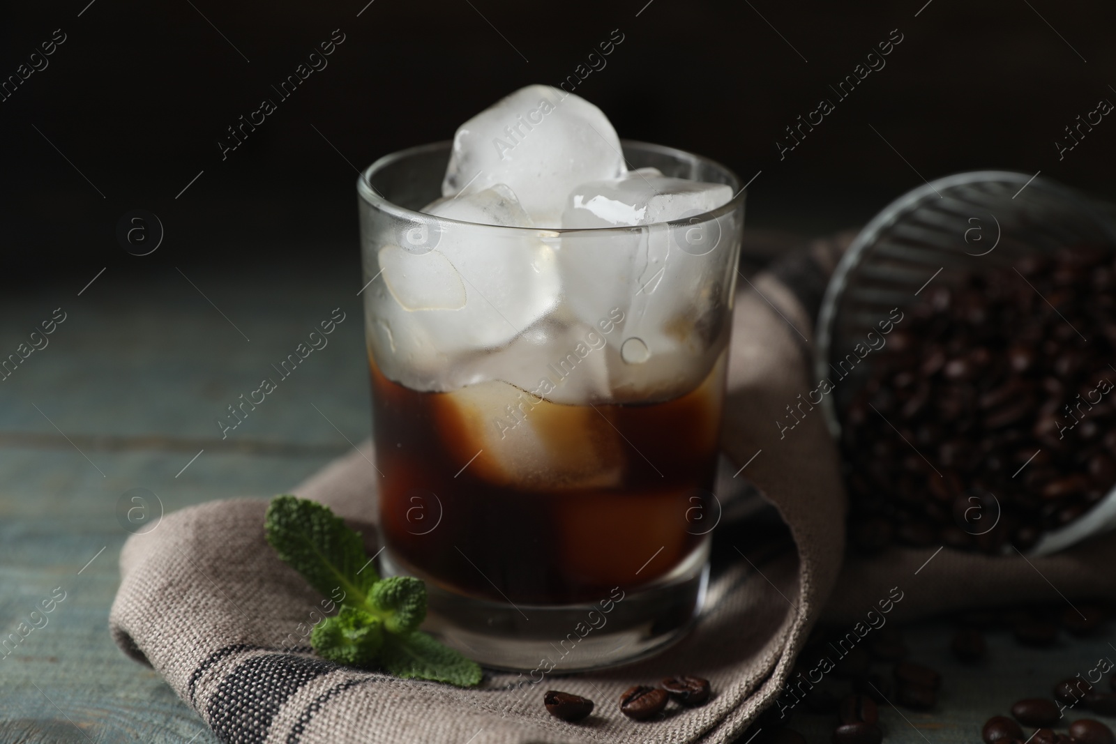 Photo of Glass of delicious iced coffee, beans and mint on light blue table, closeup