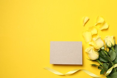 Beautiful roses, petals and blank card on yellow background, flat lay. Space for text