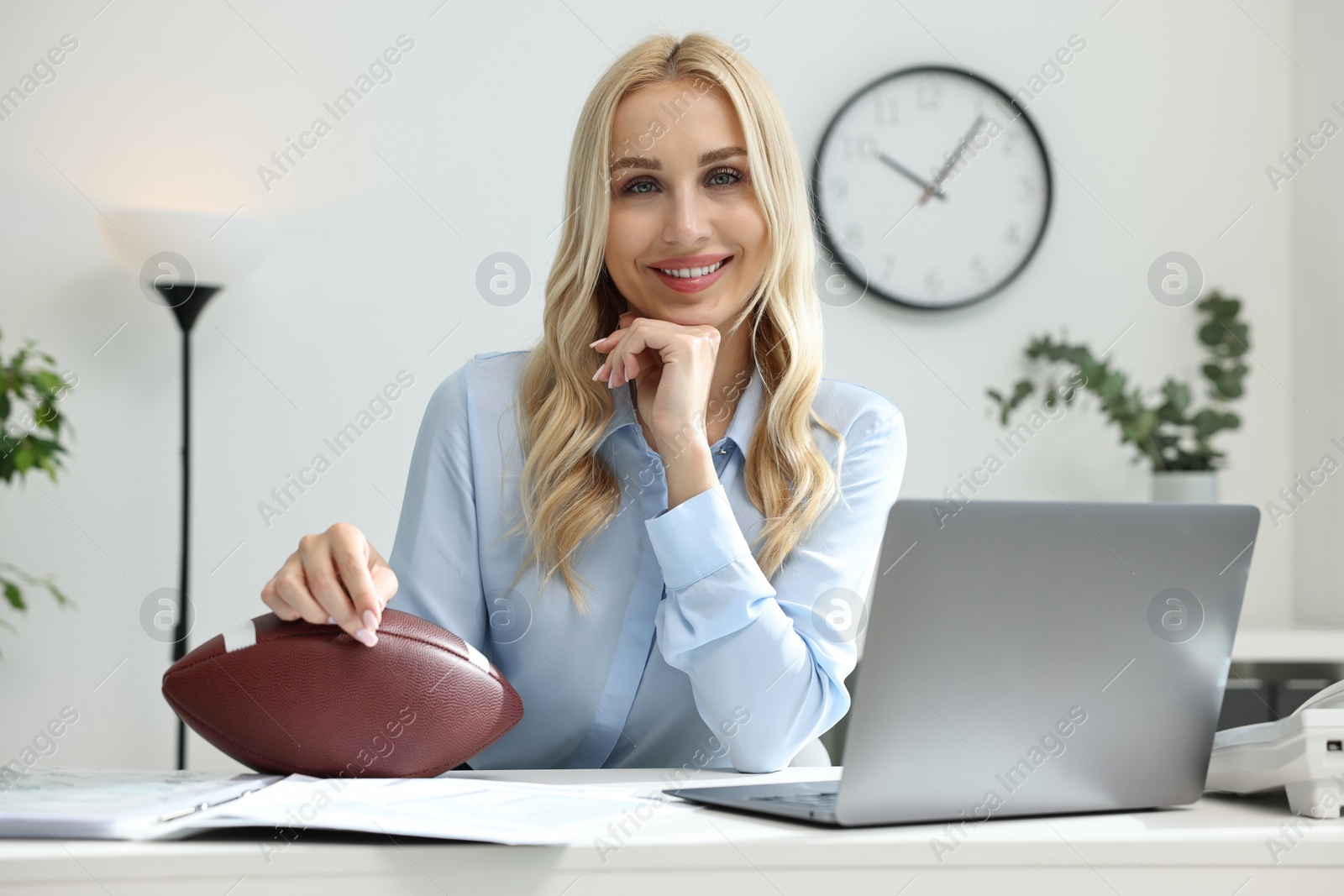 Photo of Happy woman with american football ball at table in office