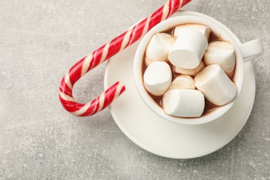 Photo of Tasty hot chocolate with marshmallows and candy cane on light grey table, top view. Space for text