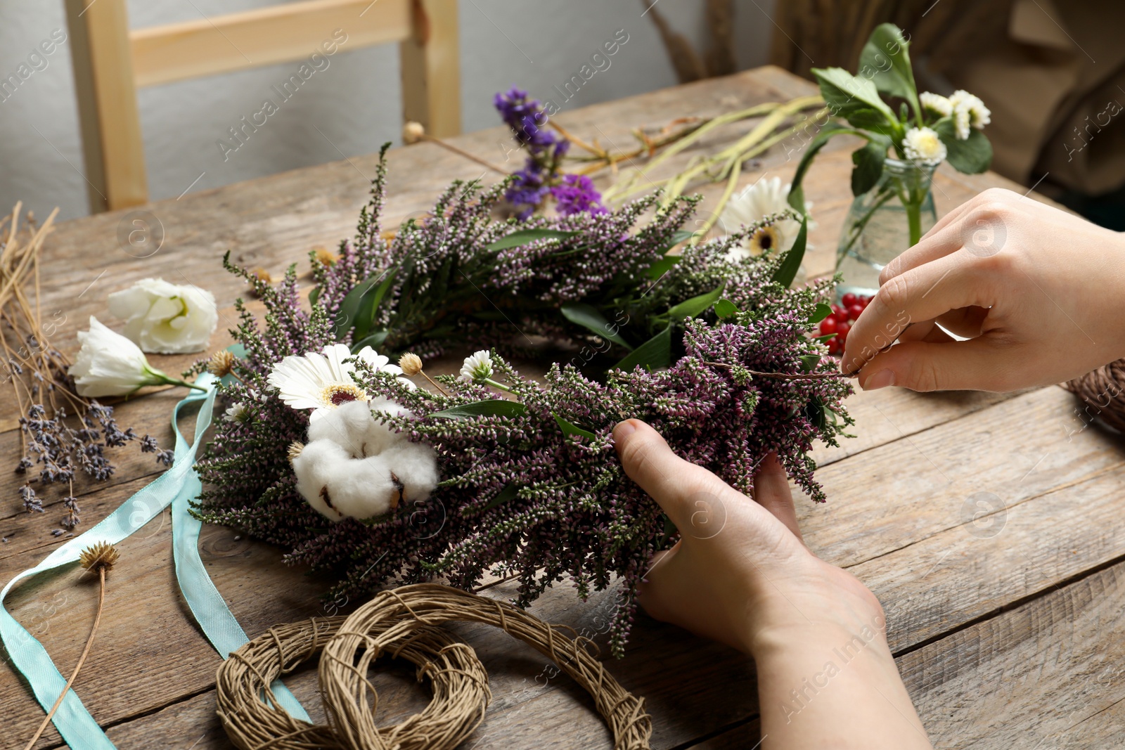 Photo of Florist making beautiful autumnal wreath with heather flowers at wooden table, closeup