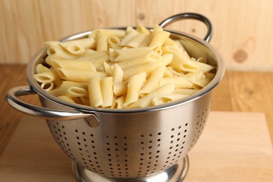 Cooked pasta in metal colander on wooden table, closeup