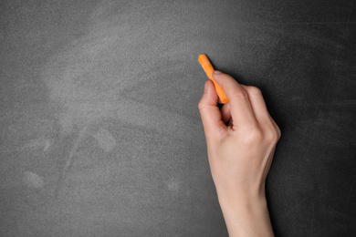 Woman with orange chalk near blackboard, closeup. Space for text