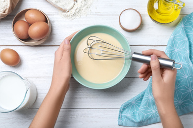 Photo of Woman preparing batter for thin pancakes at white wooden table, top view