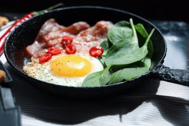 Photo of Tasty fried egg with bacon, chili pepper and spinach in pan, closeup