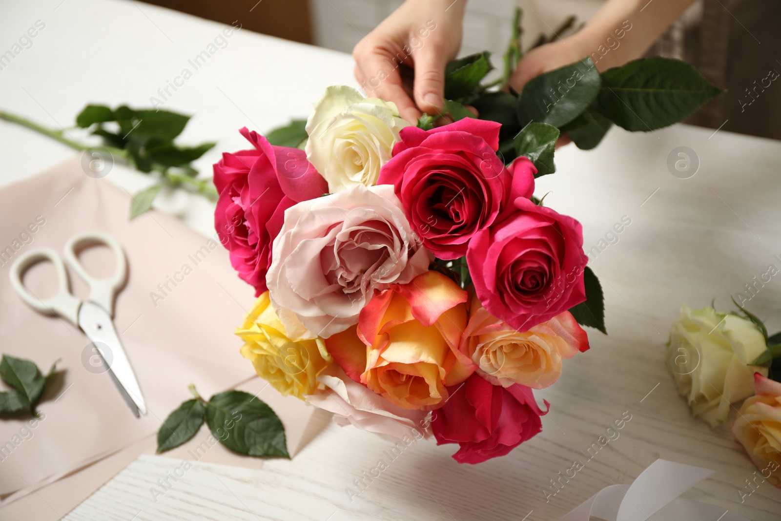 Photo of Woman making luxury bouquet of fresh roses at white wooden table, closeup