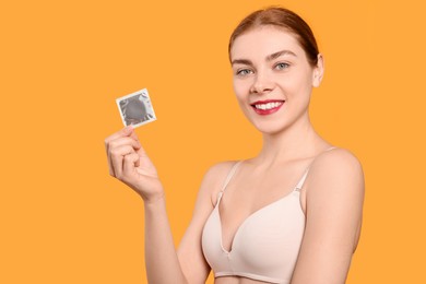 Photo of Woman in bra holding condom on yellow background, space for text. Safe sex