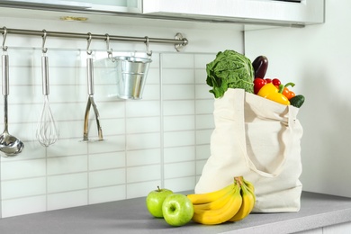 Textile shopping bag full of vegetables and fruits on countertop in kitchen. Space for text