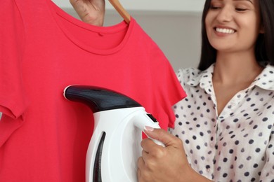 Photo of Woman steaming red t-shirt at home, closeup