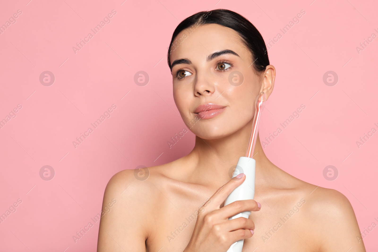 Photo of Woman using high frequency darsonval device on pink background. Space for text