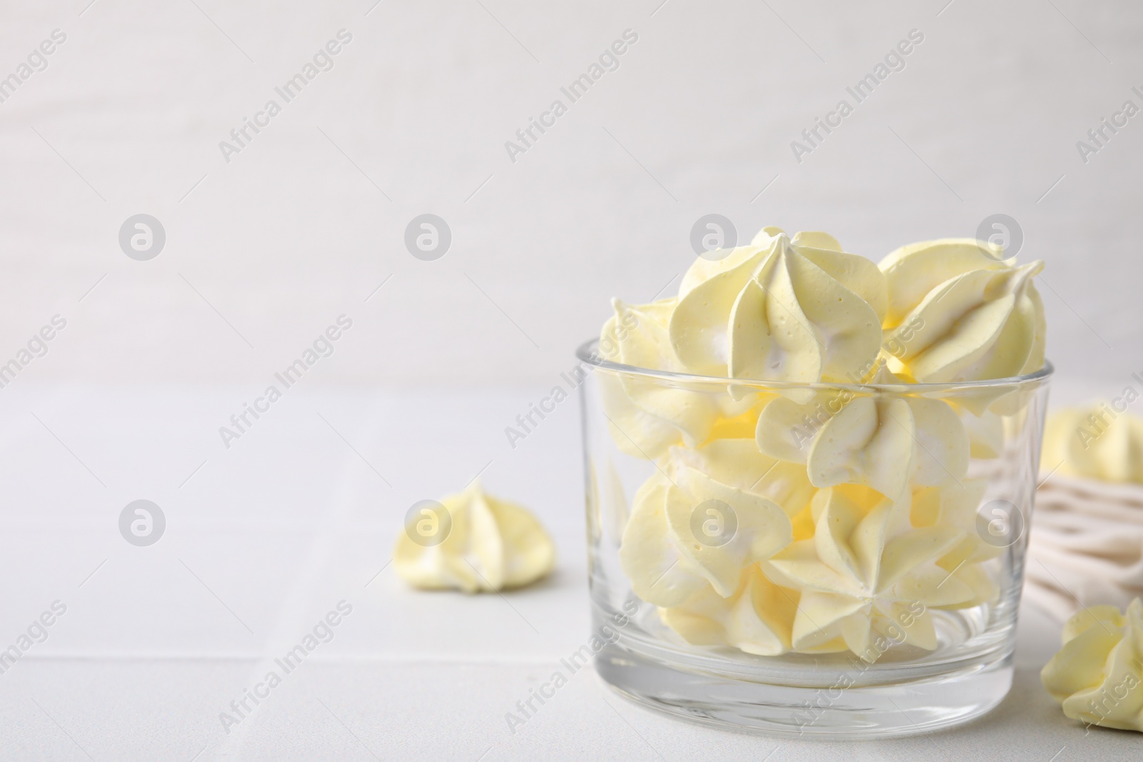 Photo of Tasty meringue cookies in glass on white tiled table. Space for text