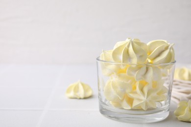 Photo of Tasty meringue cookies in glass on white tiled table. Space for text