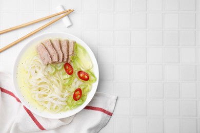 Bowl of delicious rice noodle soup with celery and meat on white tiled table, flat lay. Space for text