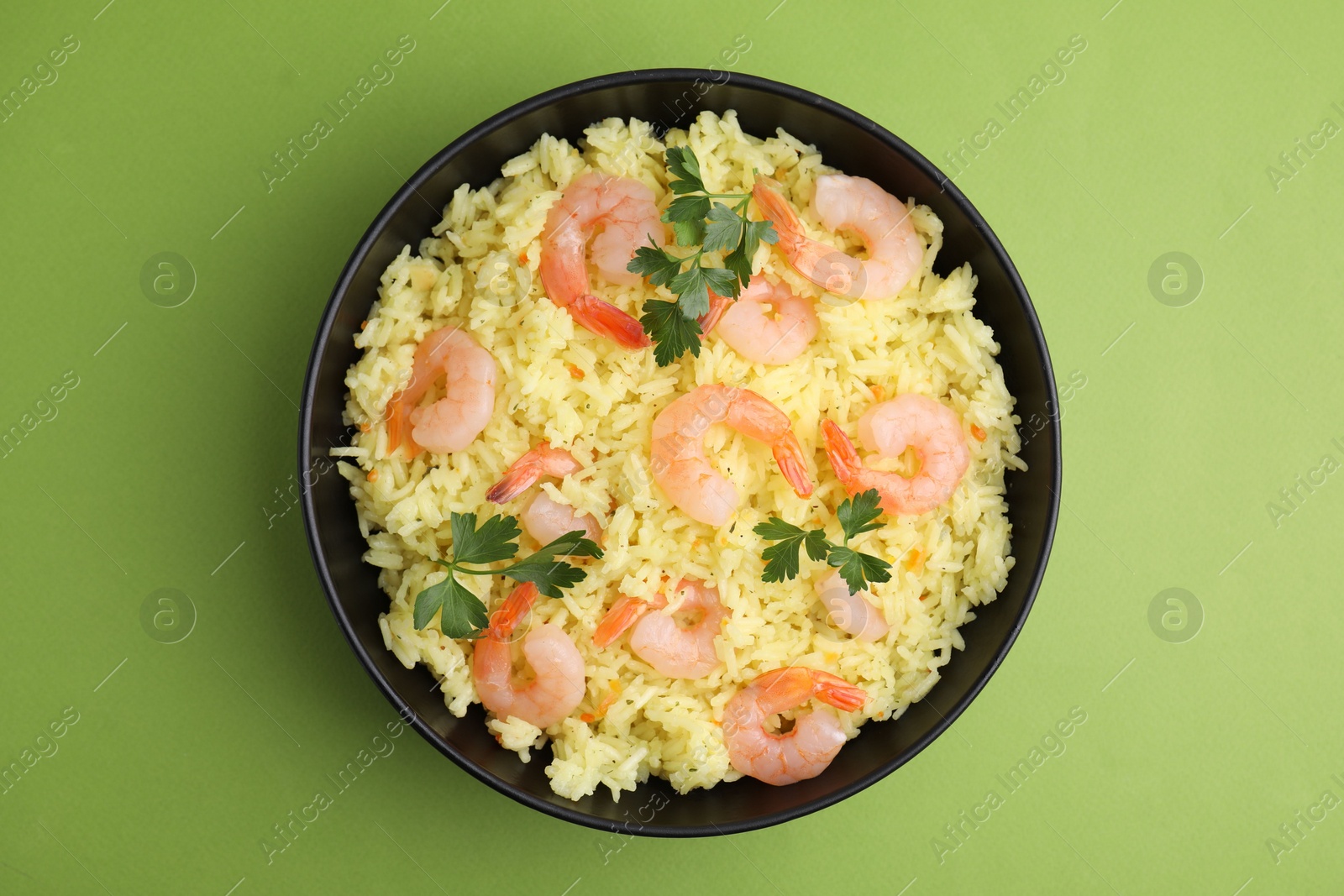 Photo of Delicious risotto with shrimps and parsley in bowl on light green background, top view