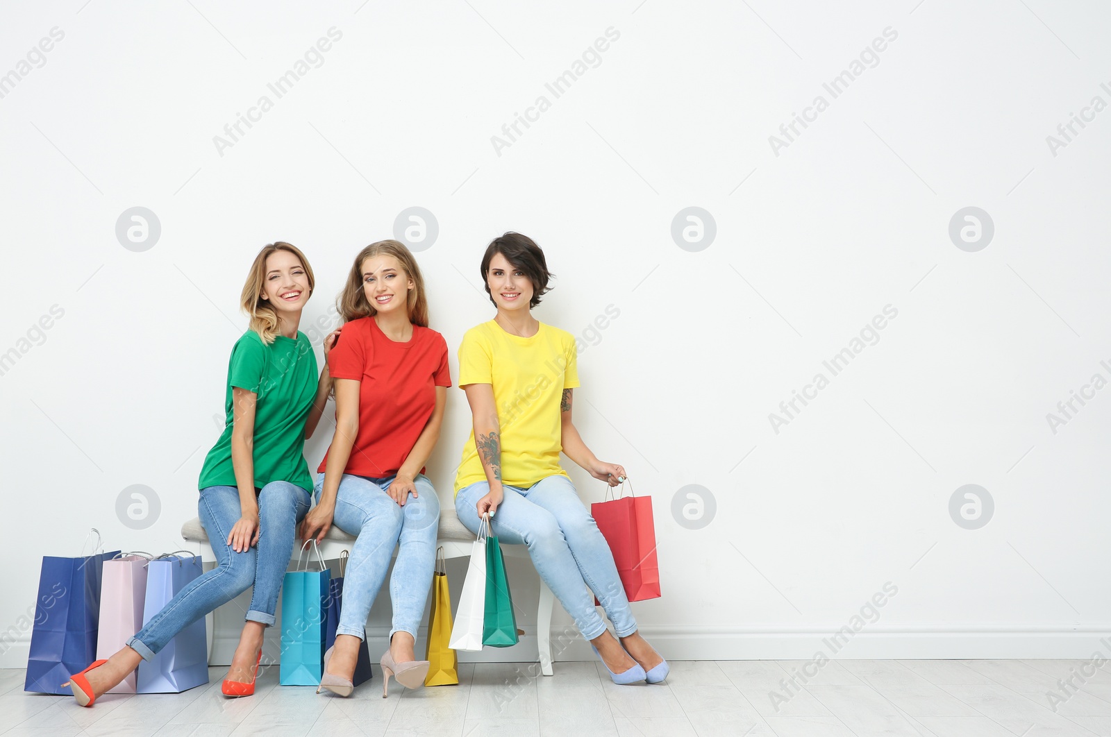 Photo of Group of young women with shopping bags sitting on ottoman near light wall