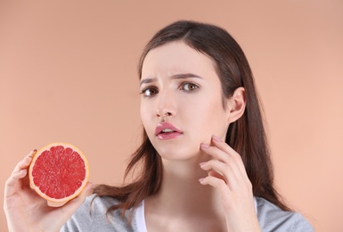 Photo of Teenage girl with acne problem holding grapefruit against color background