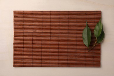 Bamboo mat and green leaves on beige table, top view. Space for text
