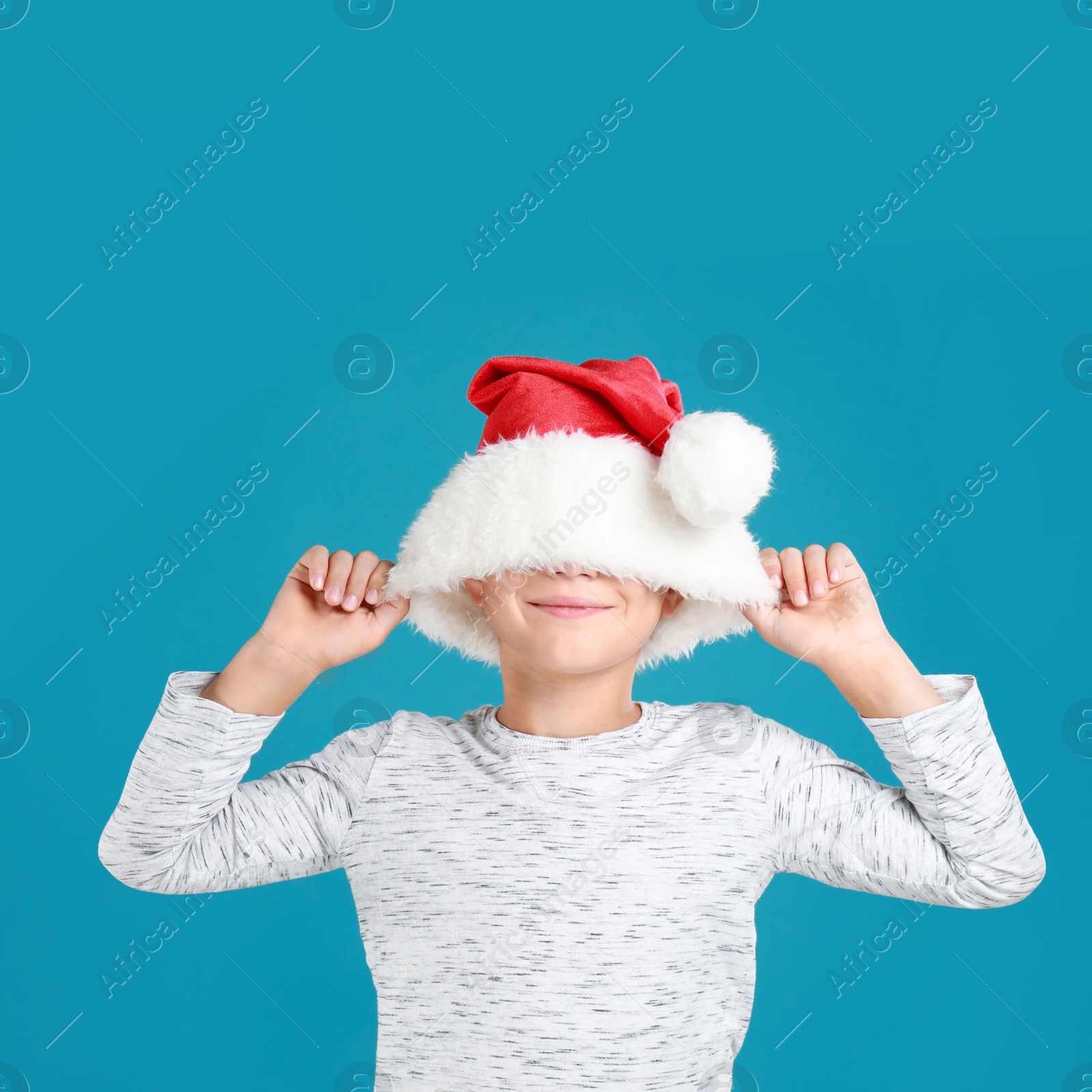 Image of Happy little child in Santa hat on light blue background. Christmas celebration