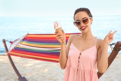 Photo of Young woman eating ice cream near hammock at seaside