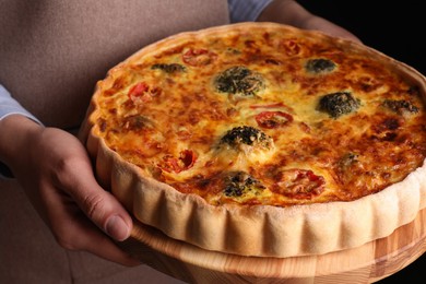 Photo of Woman holding delicious homemade vegetable quiche on black background, closeup