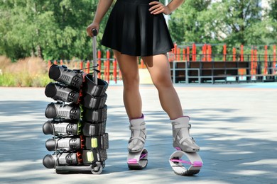 Photo of Woman with kangoo jumping boots on hand trolley outdoors, closeup