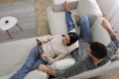Couple with tablet resting on sofa in living room, above view