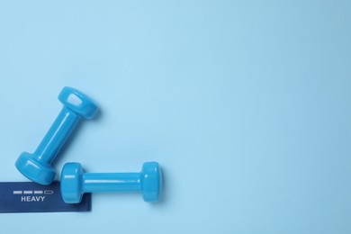 Photo of Two dumbbells and fitness elastic band on light blue background, flat lay. Space for text