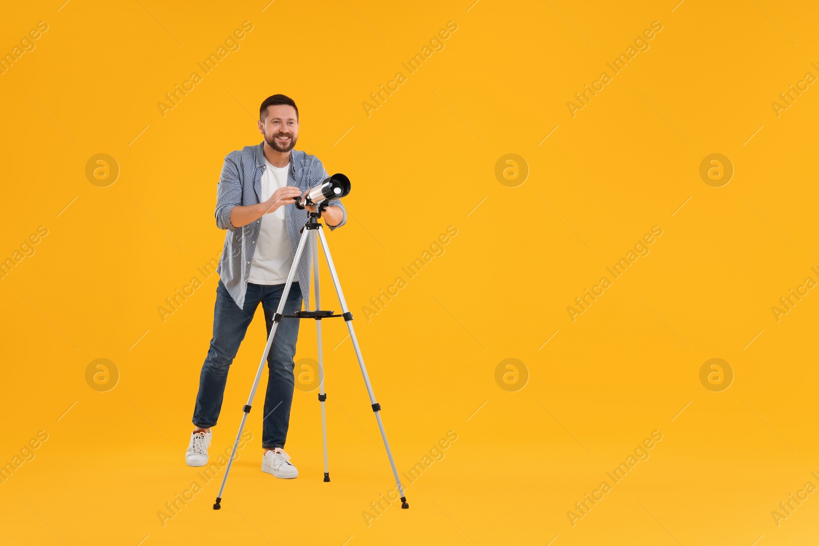 Photo of Happy astronomer with telescope on orange background. Space for text