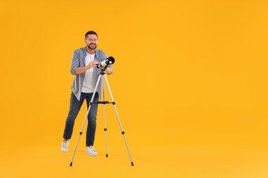 Photo of Happy astronomer with telescope on orange background. Space for text