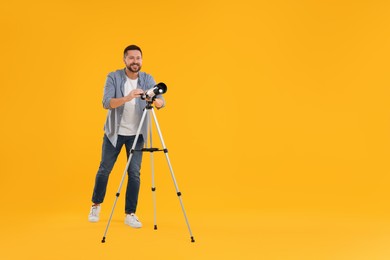 Happy astronomer with telescope on orange background. Space for text