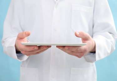 Photo of Doctor with tablet on light blue background, selective focus